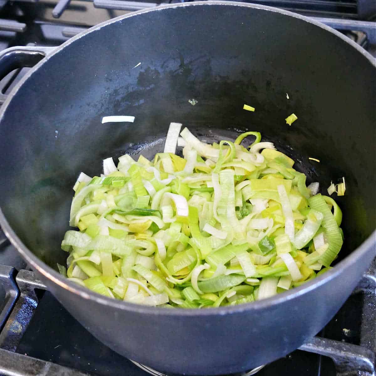 sliced leeks cooking in olive oil in a large soup pot on a stove