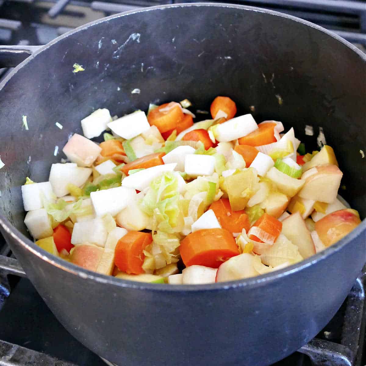 leeks, turnips, carrots, and apples cooking in a soup pot on a stove