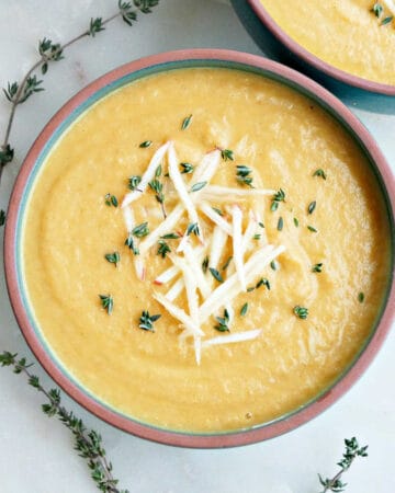 bowl of carrot turnip soup with matchstick apples and thyme on a counter