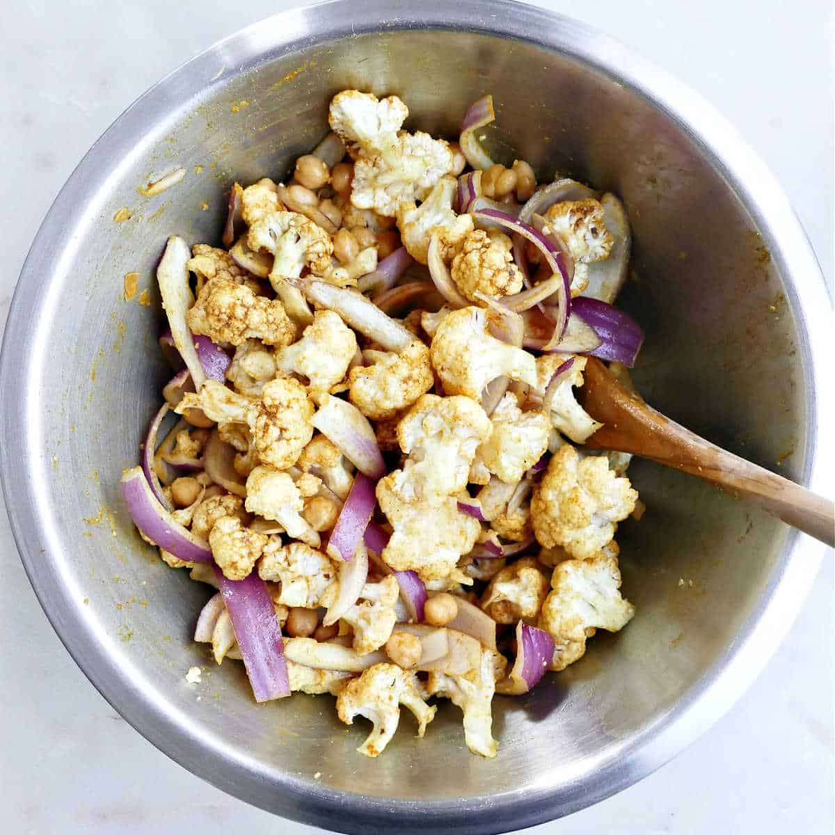 cauliflower, chickpeas, and red onions tossed with seasonings in a bowl