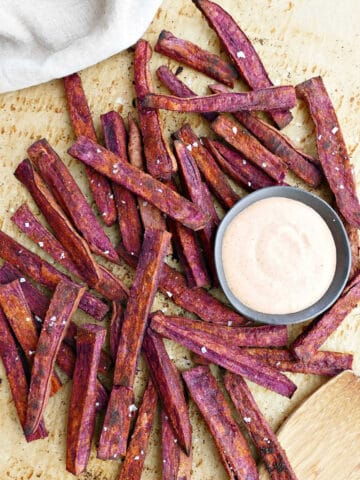 purple sweet potato fries with dipping sauce on a piece of parchment paper
