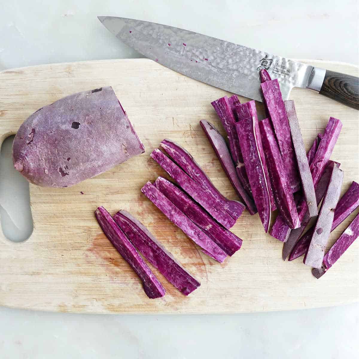 purple sweet potato being cut into fries on a cutting board with a knife
