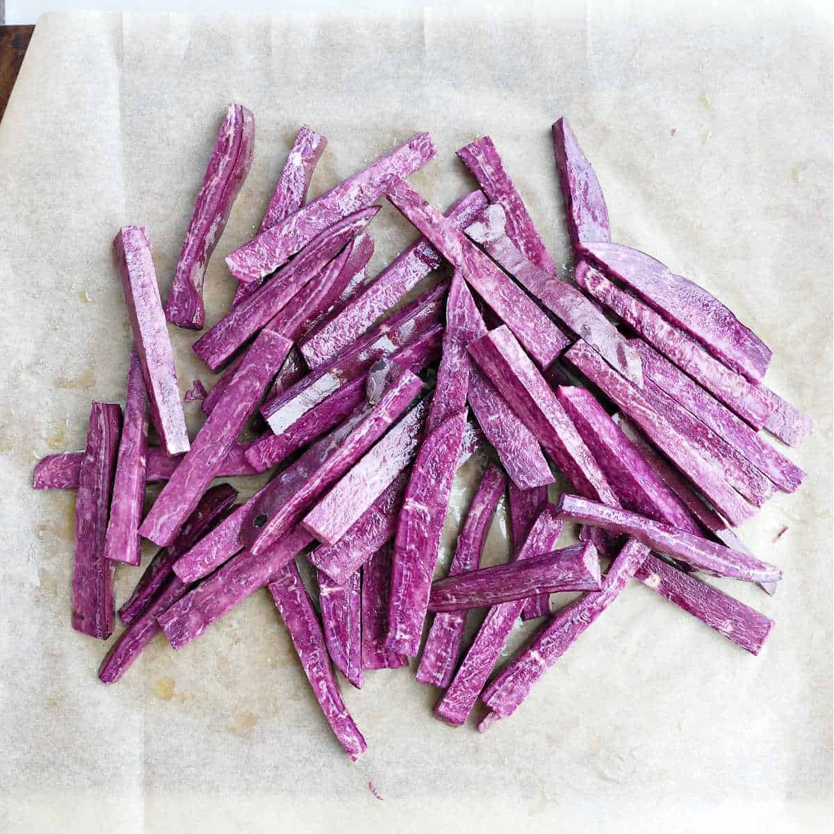 purple potato sticks tossed with olive oil on the center of parchment paper