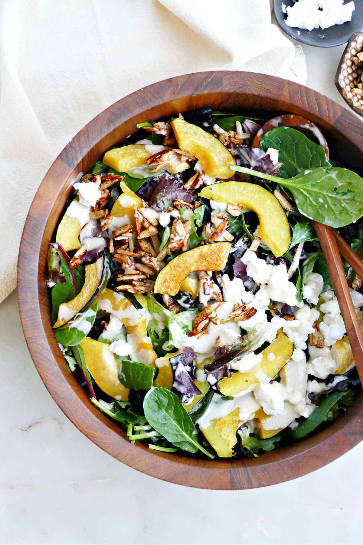 roasted acorn squash with salad greens and tahini dressing in a bowl with tongs