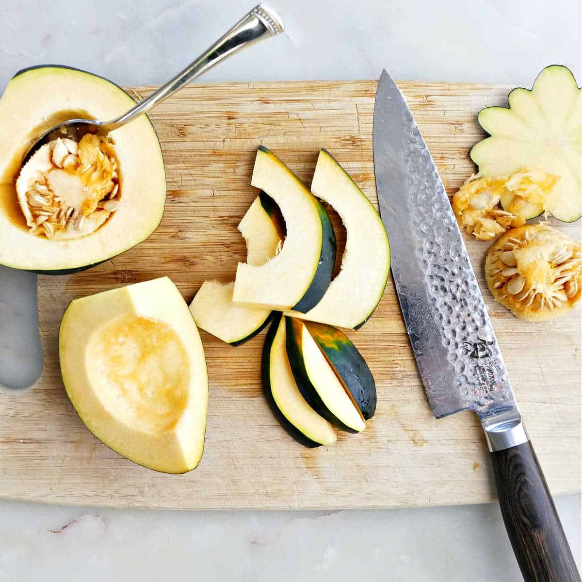 acorn squash being deseeded and sliced on a cutting board with a knife