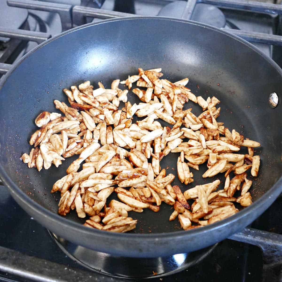 slivered almonds cooking in maple syrup and cinnamon in a skillet