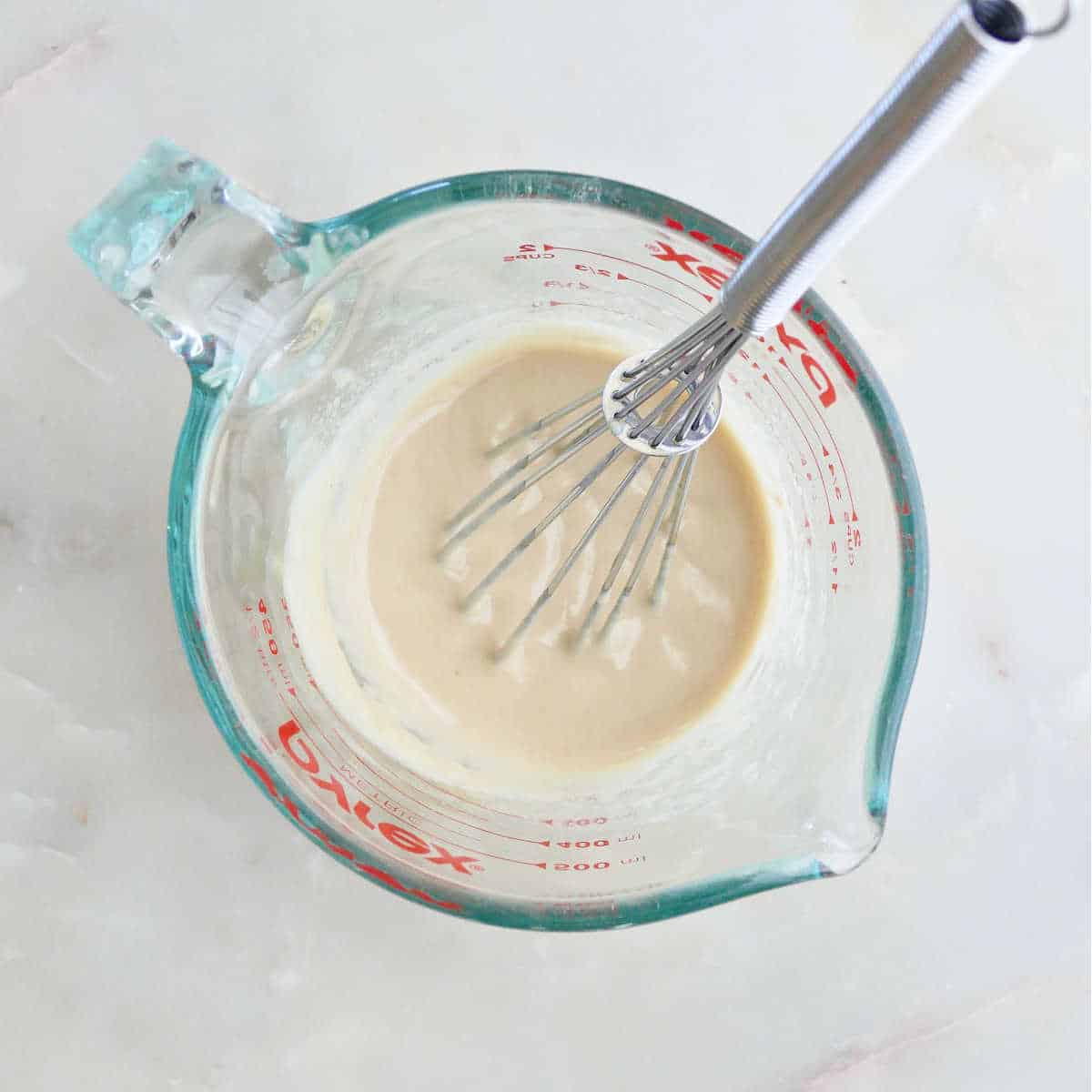 ingredients for tahini dressing being whisked together in a glass measuring cup