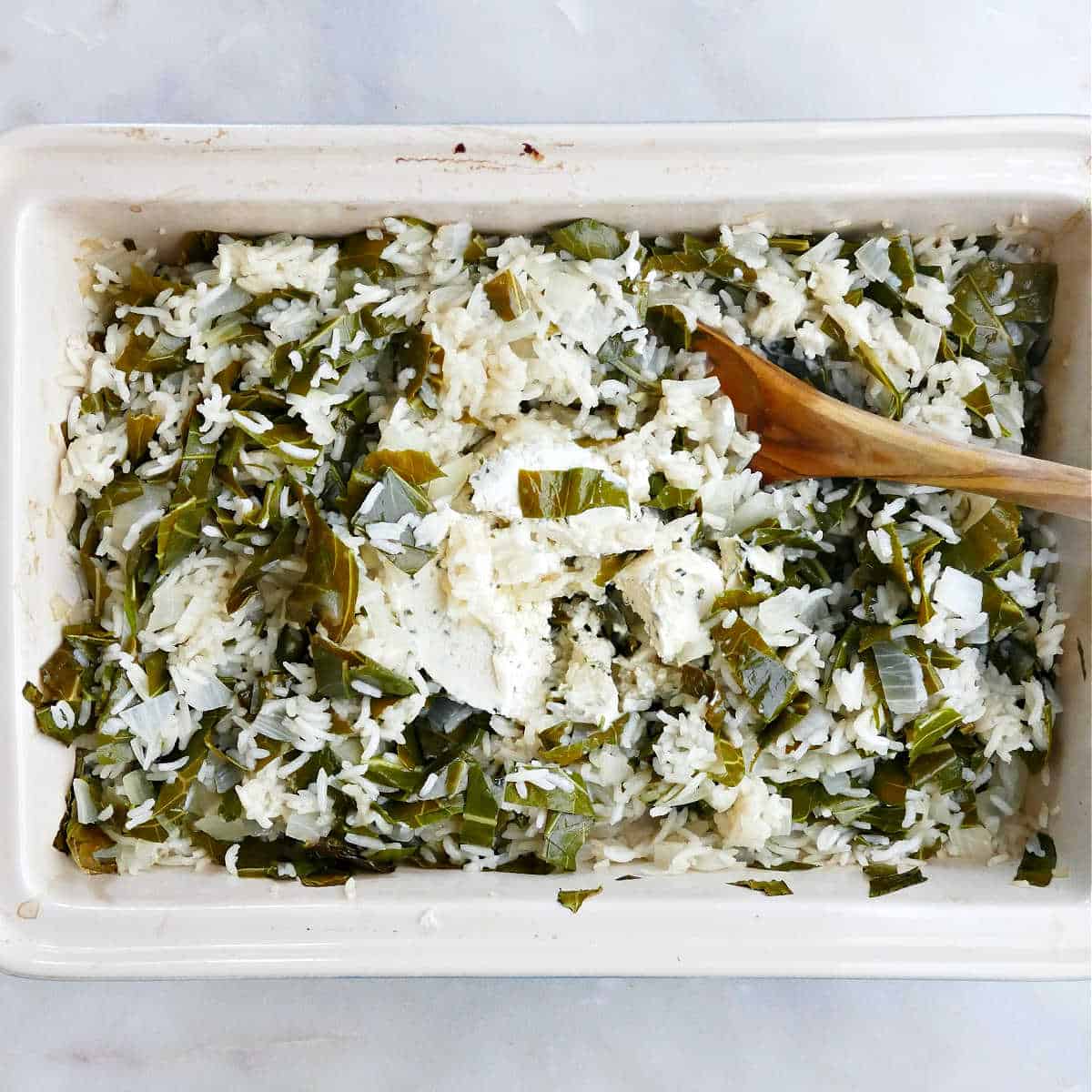 Boursin cheese being stirred into collard greens and rice with a spoon in a dish