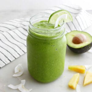 green smoothie in a glass with ingredients and a napkin scattered around it