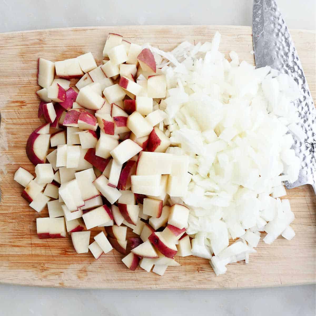 diced onion and cubed red potato on a cutting board with a knife