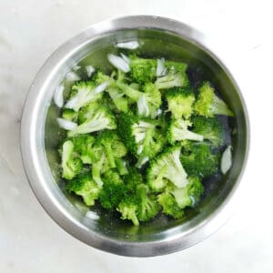 blanched broccoli in a mixing bowl of ice water on a counter