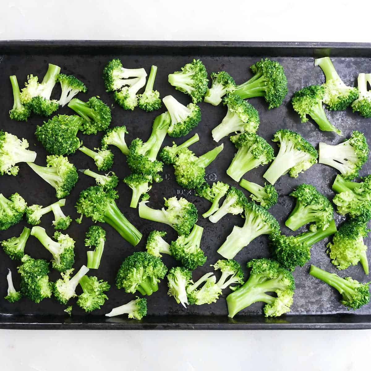 blanched broccoli spread out on a baking sheet on a counter