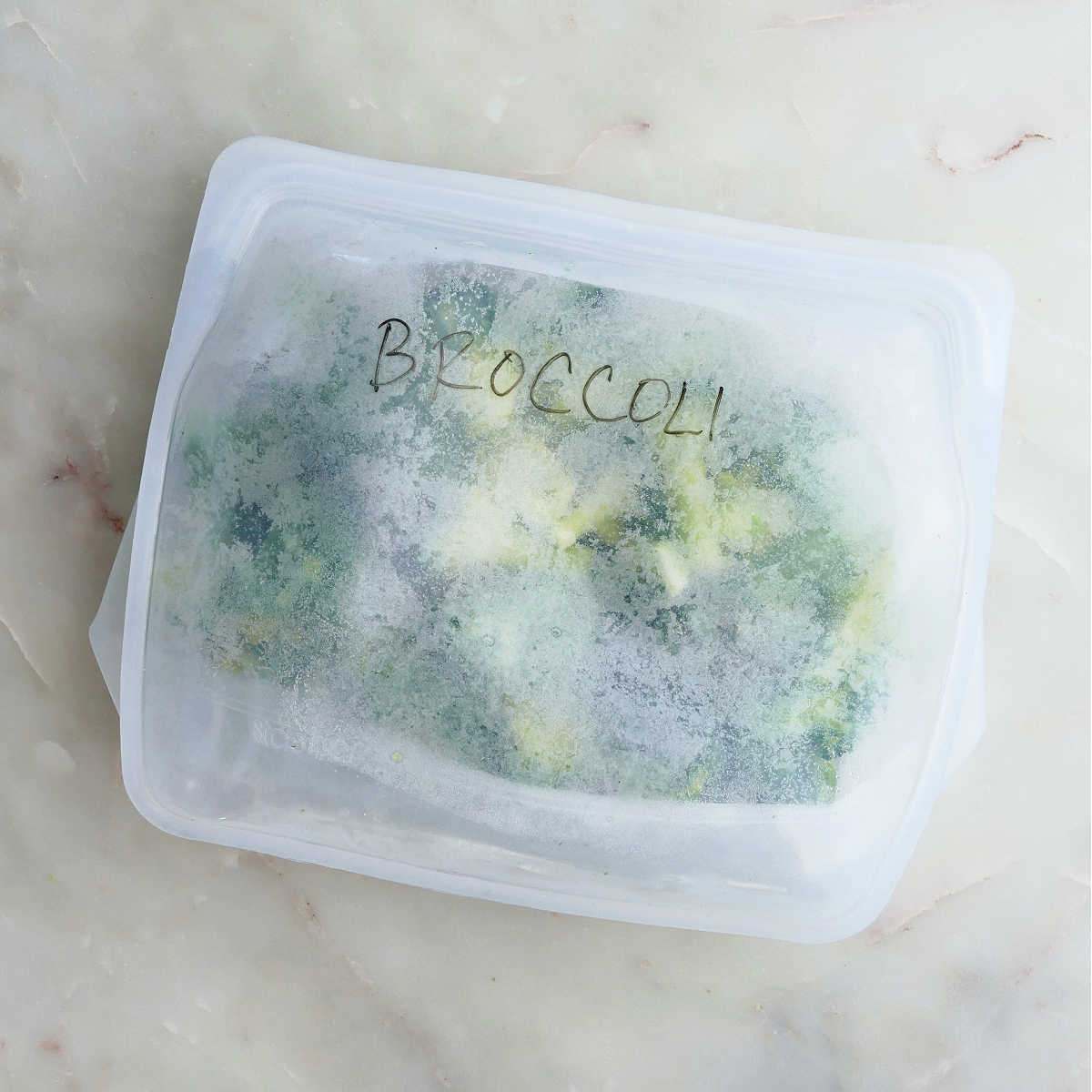 blanched broccoli in a labeled silicone freezer bag on a counter
