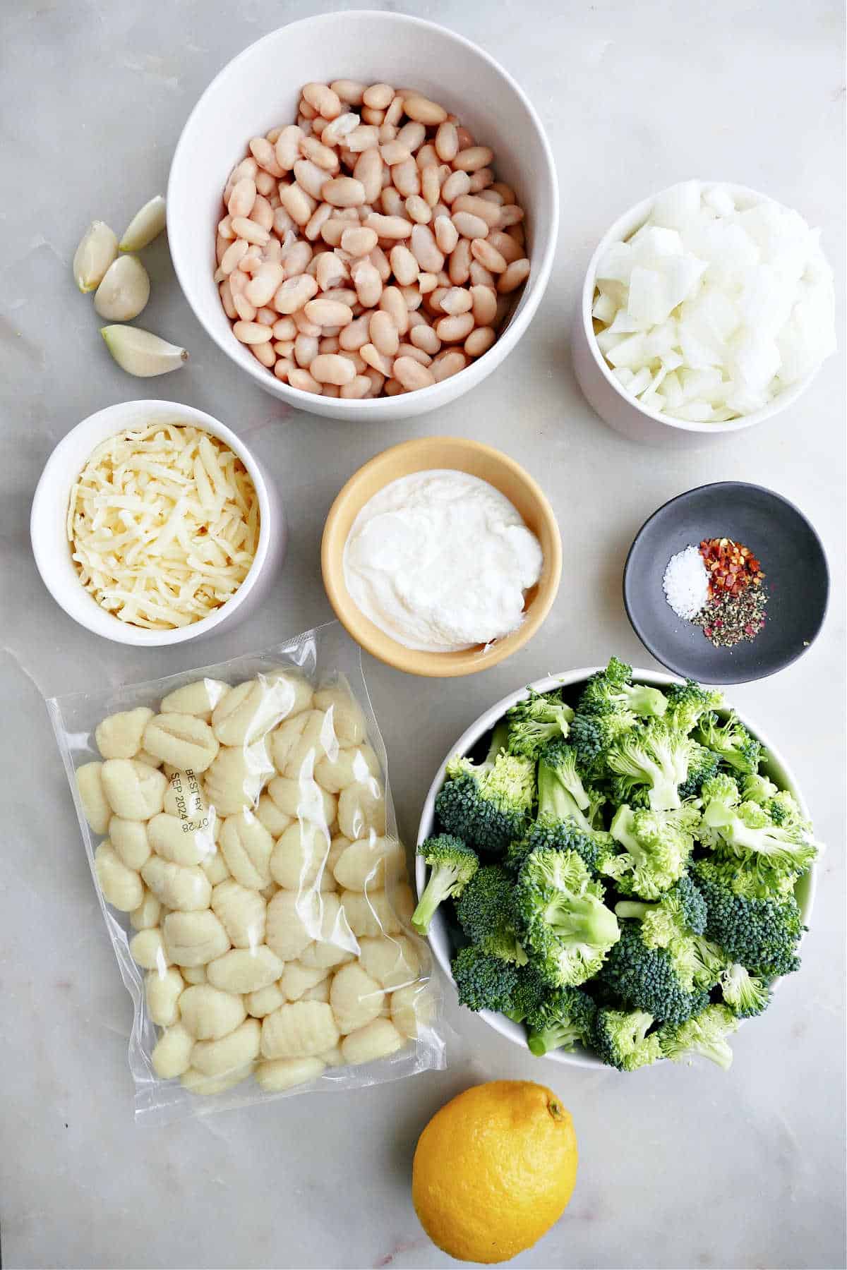 lemon, gnocchi, broccoli, cheeses, garlic, white beans, diced onion, and spices on a counter