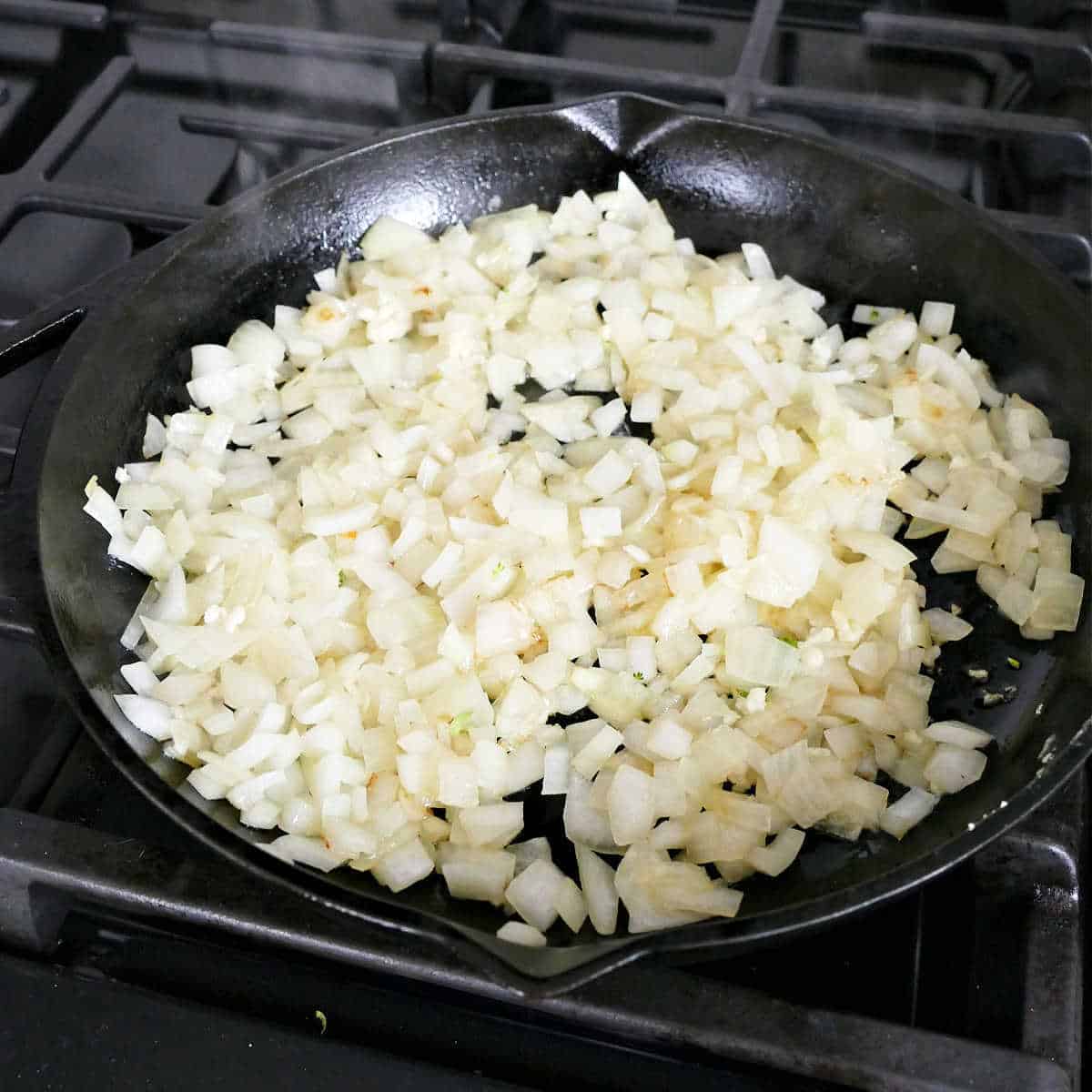 onion and garlic cooking in olive oil in a cast iron skillet on a stove