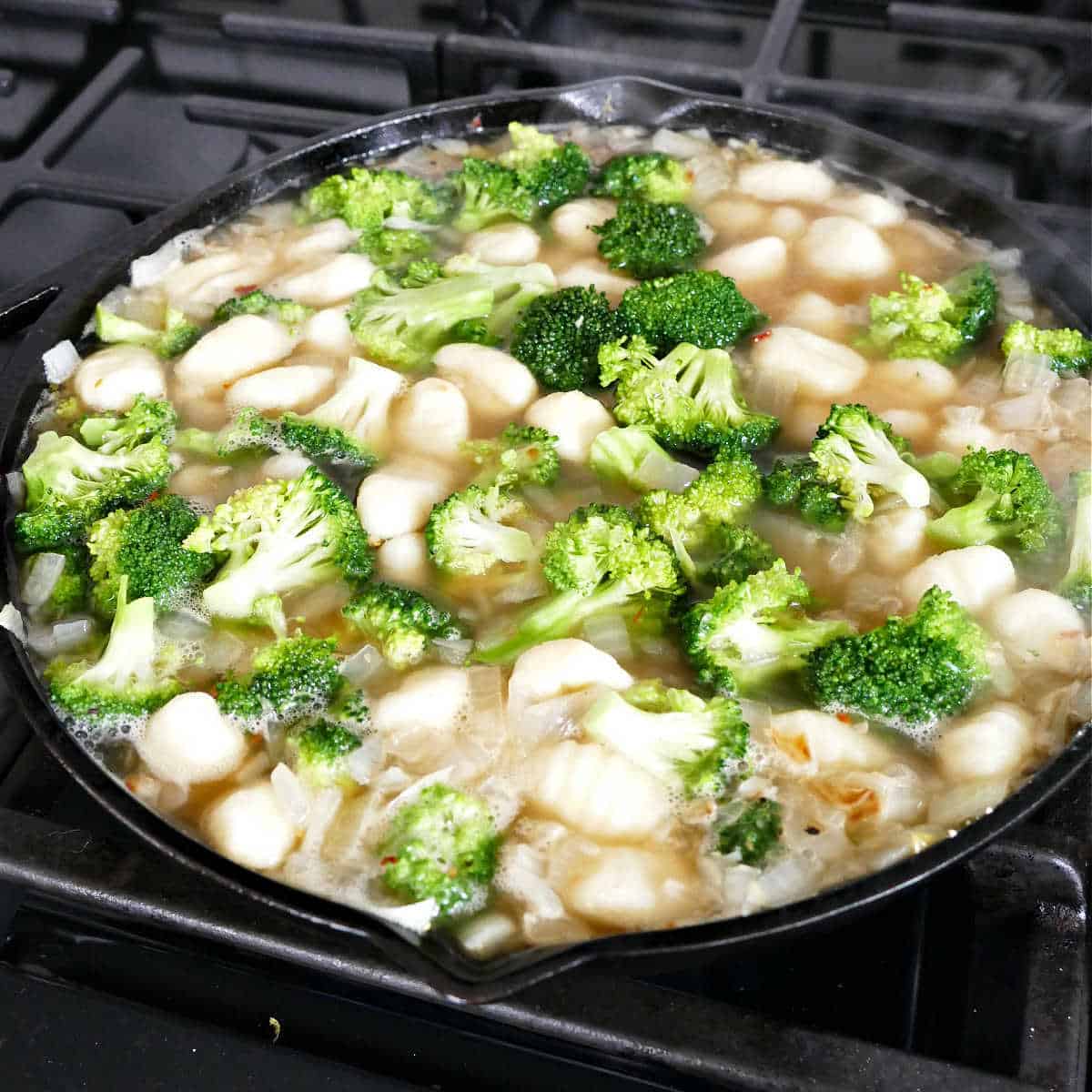 ingredients for gnocchi and broccoli cooking in a cast iron skillet on a stove