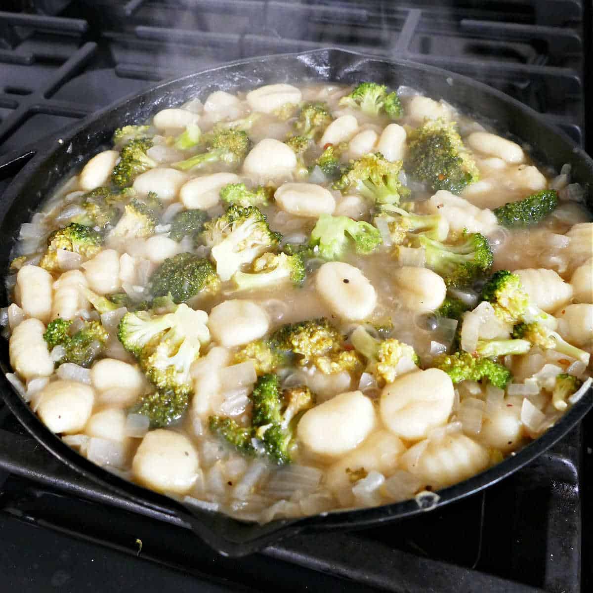 gnocchi, broccoli, vegetable broth, and seasonings cooking in a skillet on a stove