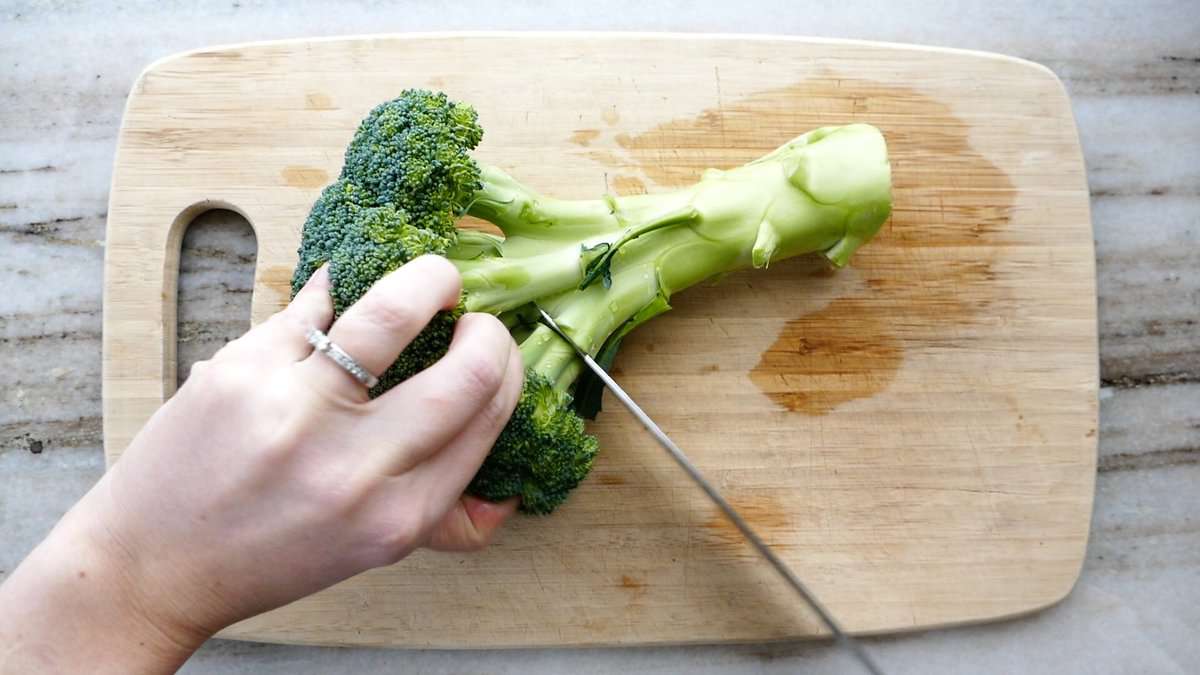 woman cutting broccoli florets off of the stem with a knife on a cutting board