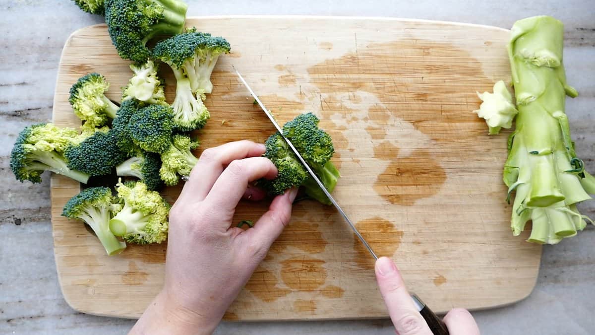 woman slicing a broccoli floret in half lengthwise on a cutting board