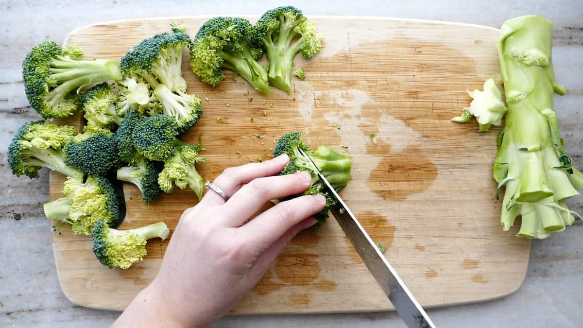woman slicing off the stem from broccoli florets to break apart into pieces