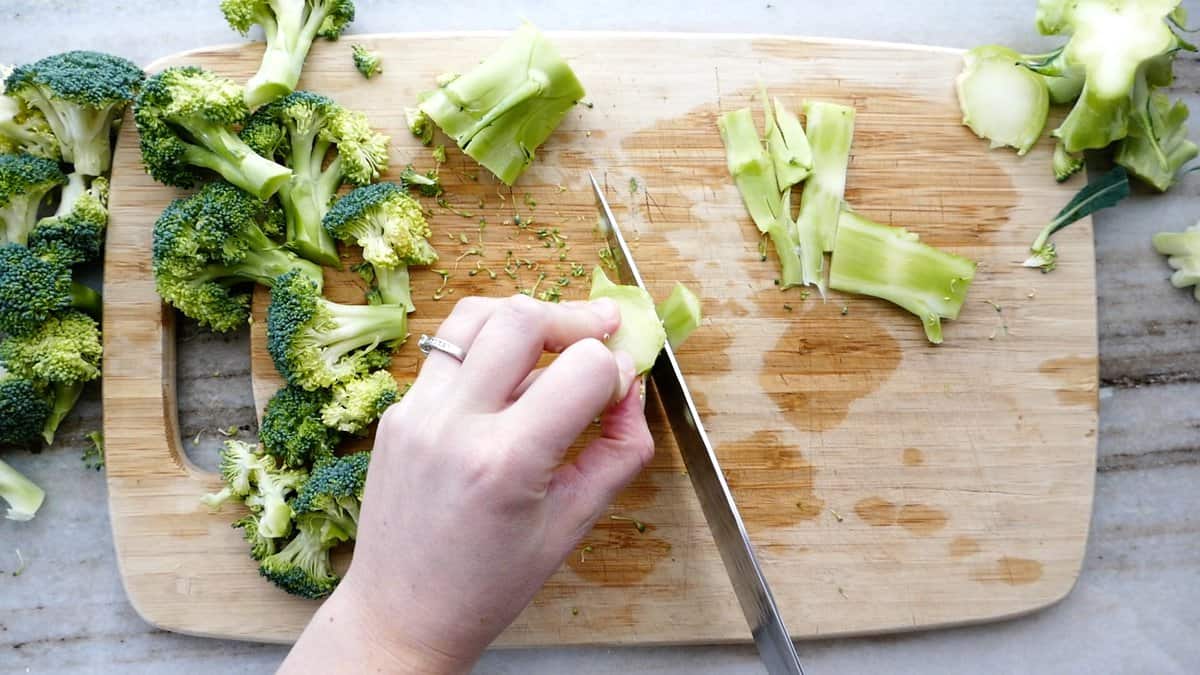 woman remove the outer skin of a broccoli stem with a knife on a cutting board