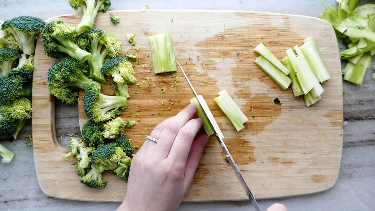 woman slicing a broccoli stem into matchstick pieces on a cutting board