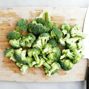 broccoli florets on a bamboo cutting board next to a knife on a counter