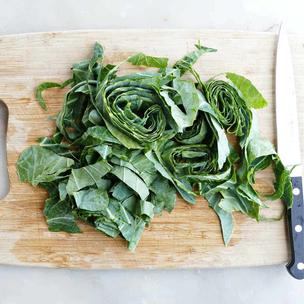 collard greens being cut into strips on a cutting board with a knife