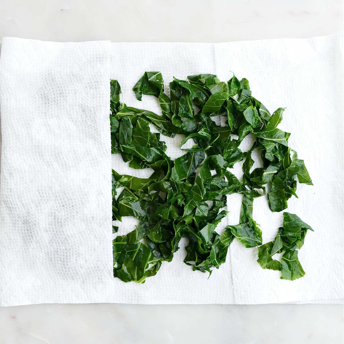 blanched collard greens being dried with paper towels on a counter