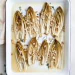 8 halves of roasted endive on a rectangular tray with pine nuts and thyme