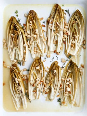 8 halves of roasted endive on a rectangular tray with pine nuts and thyme