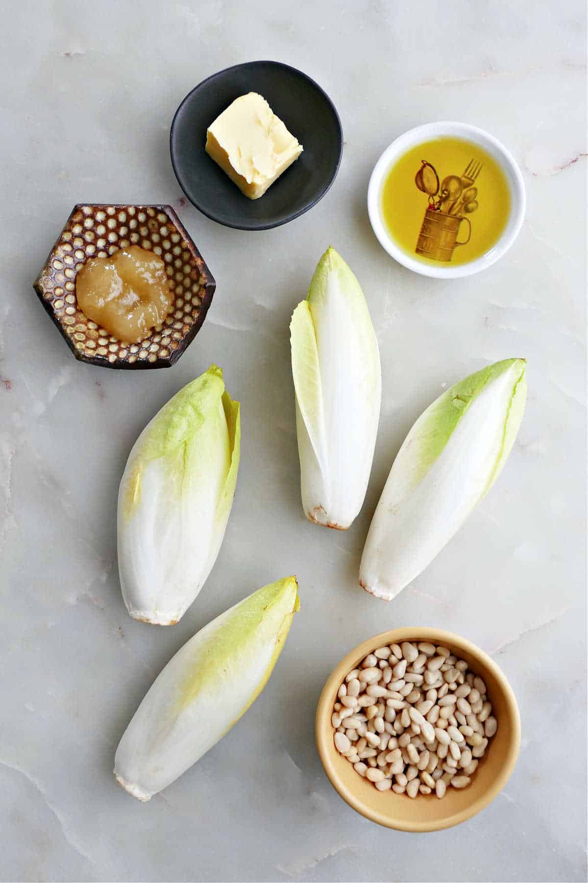 toasted pine nuts, 4 heads of Belgian endive, honey, butter, and olive oil on a counter