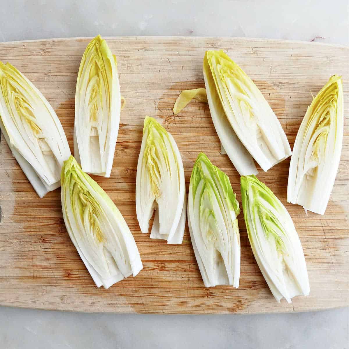 heads of endive sliced in half lengthwise with cores removed on a cutting board