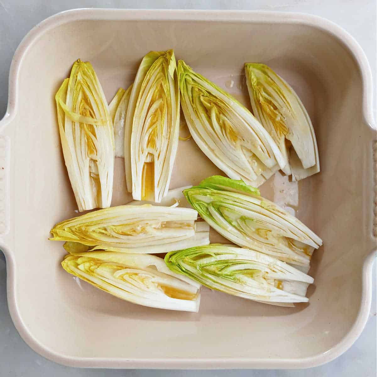 8 halves of Belgian endive topped with honey butter in a baking dish before being roasted