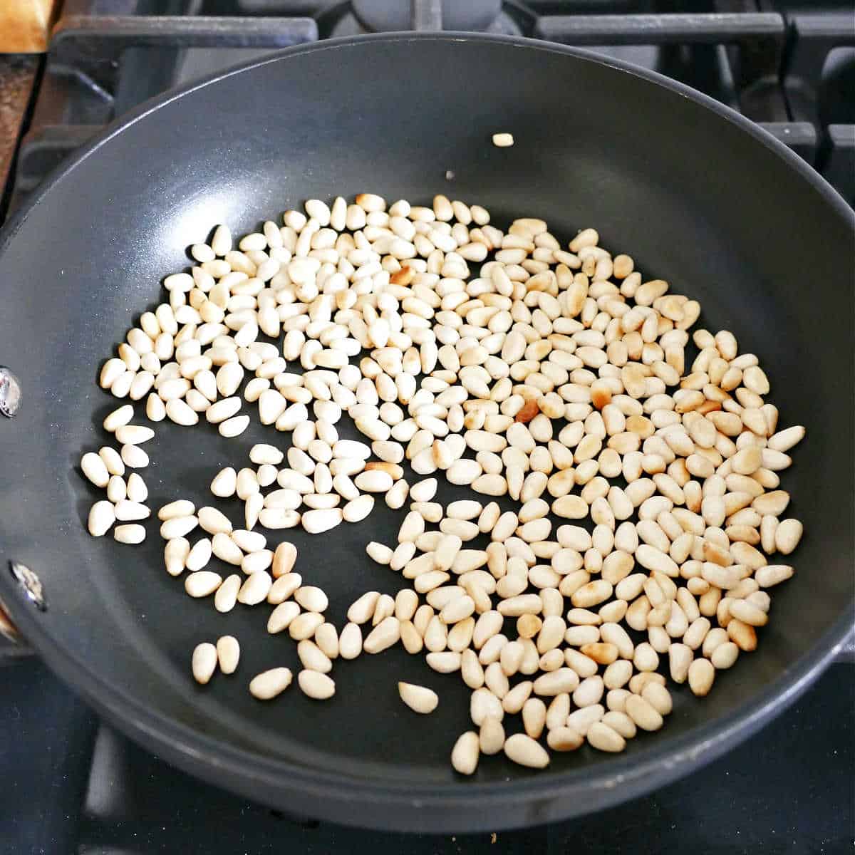 pine nuts being toasted until fragrant in a skillet on a stove