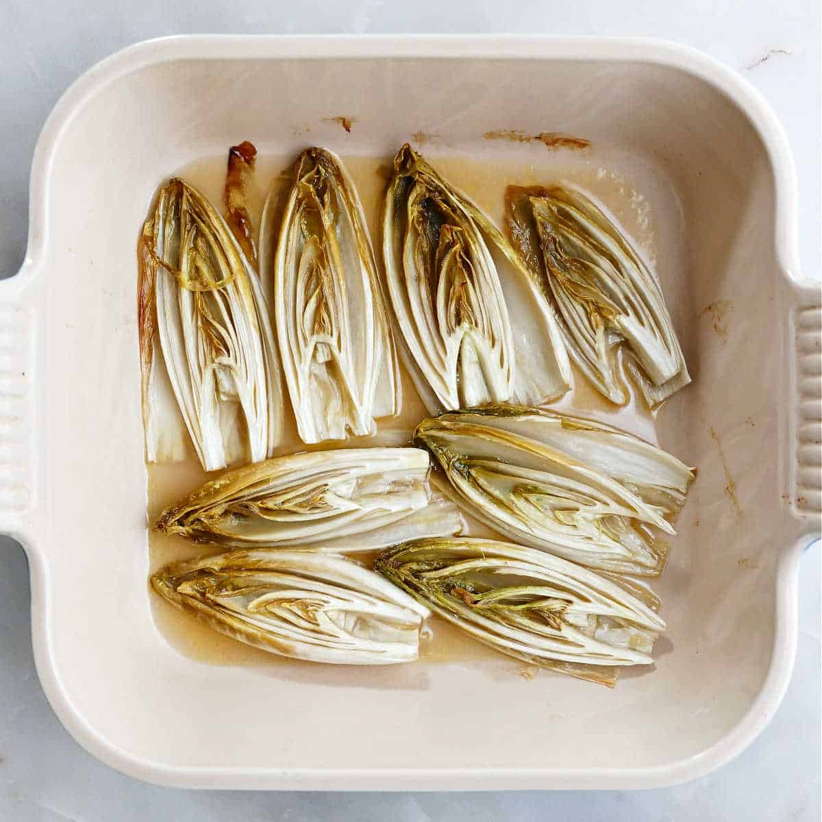 roasted endive in a baking dish with a mixture of butter, honey, and olive oil