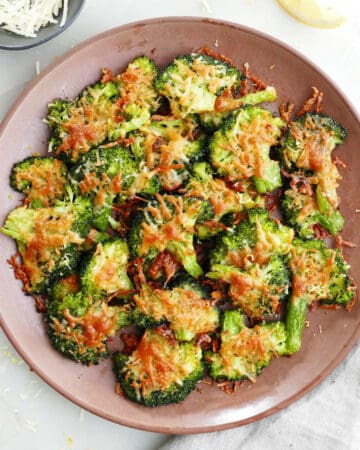 smashed broccoli with parmesan cheese on a plate next to napkin and garnishes