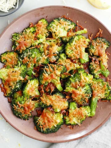 smashed broccoli with parmesan cheese on a plate next to napkin and garnishes
