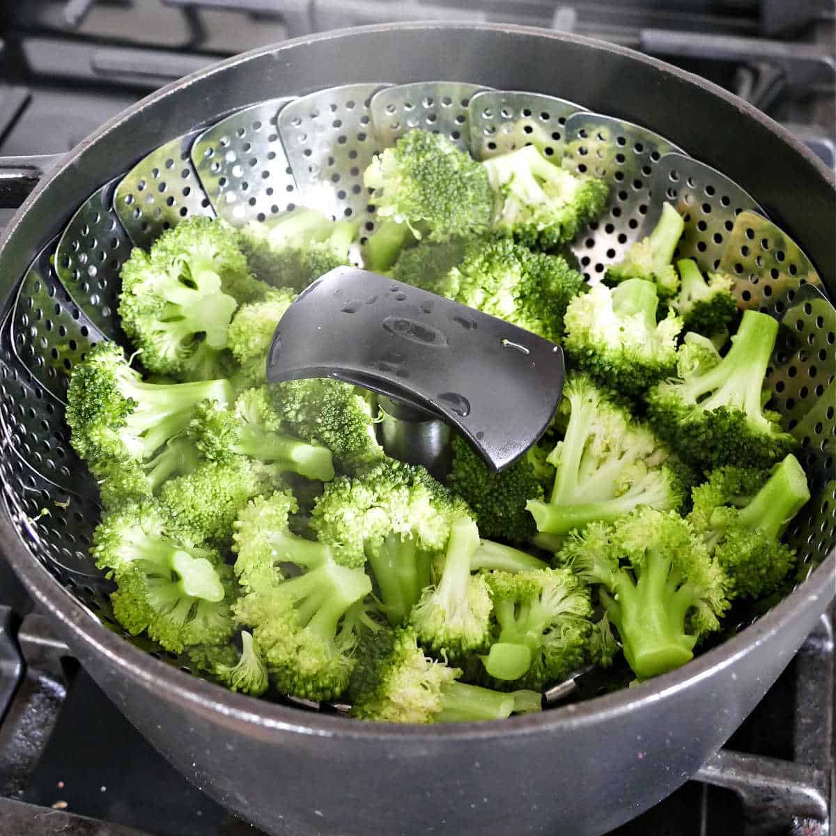 broccoli florets cooking in a vegetable steamer basket in a pot on a stove