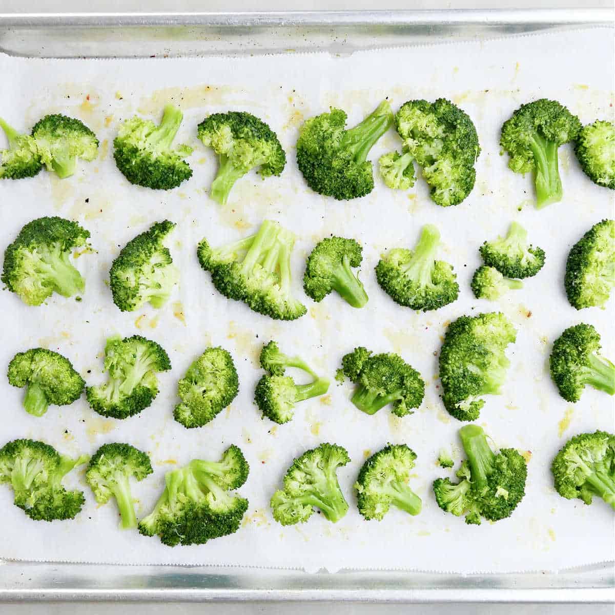 steamed broccoli smashed into flat pieces on a lined baking sheet