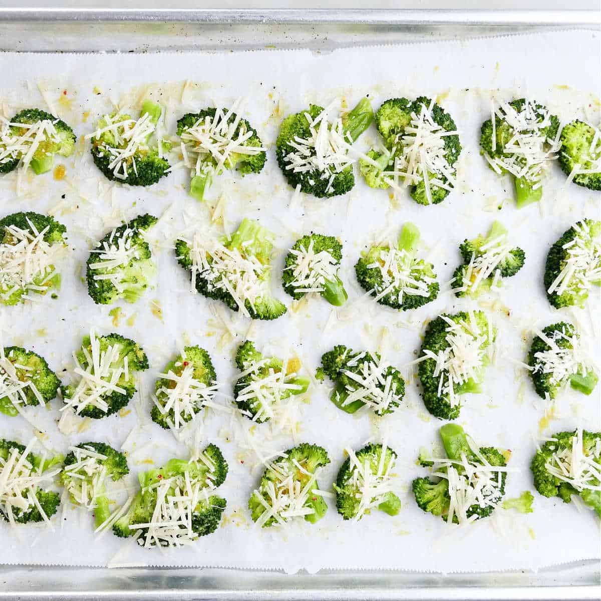 smashed broccoli pieces topped with parmesan cheese on a baking sheet before going in the oven