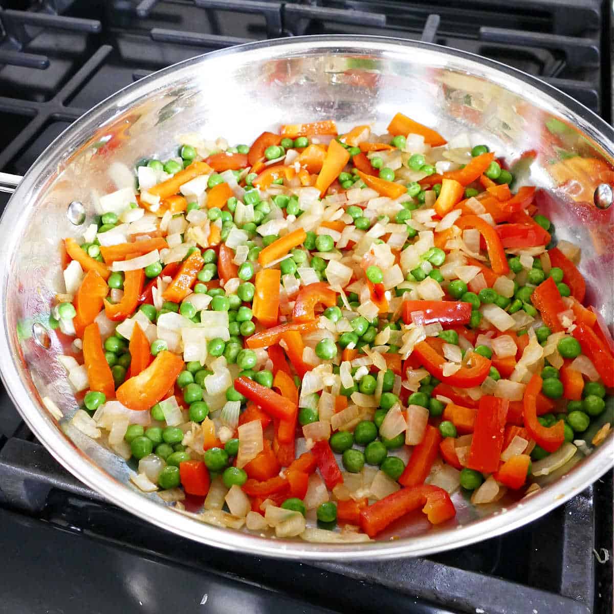 onion, bell pepper, and peas in a skillet cooking with olive oil