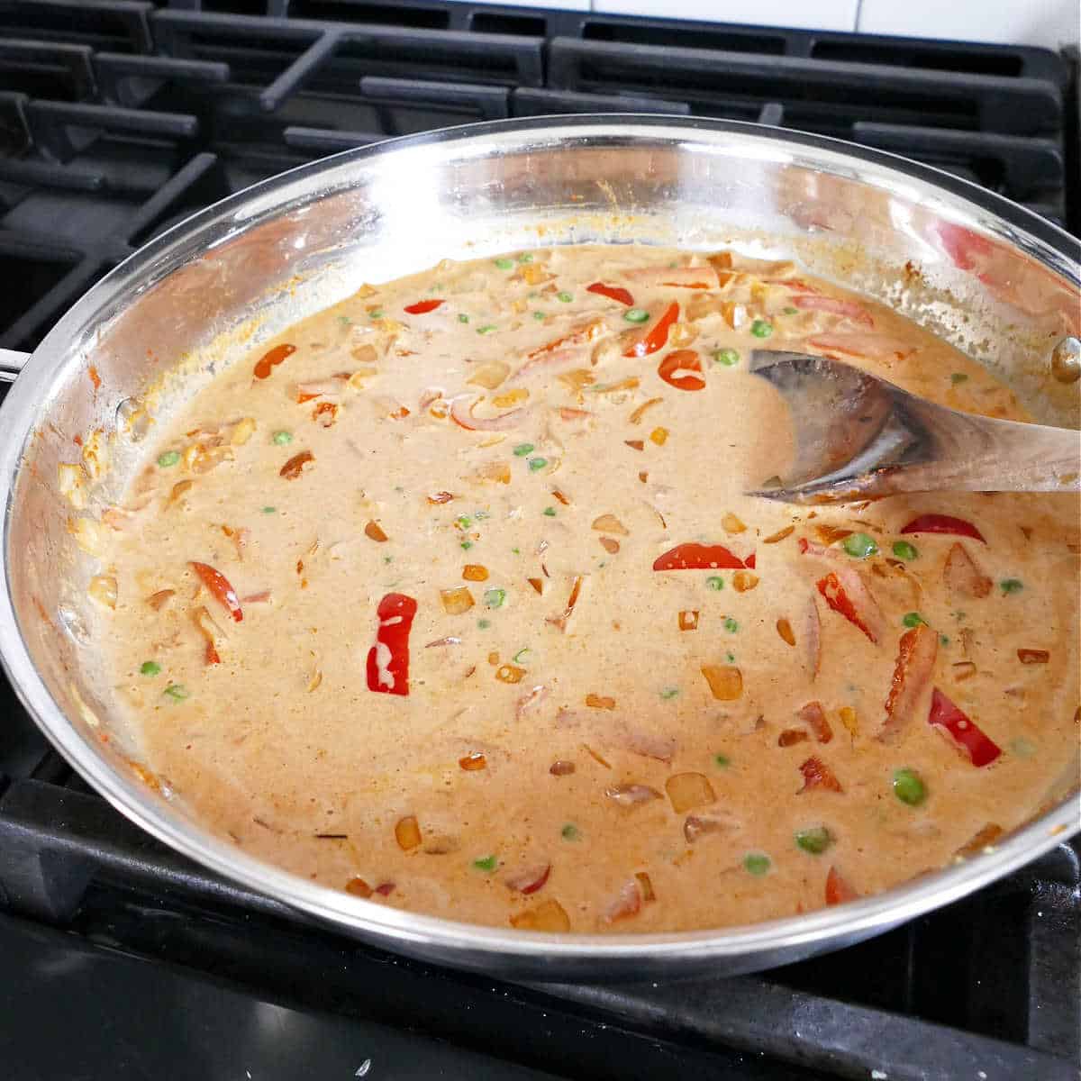 coconut milk being stirred into a skillet of vegetables and red curry paste