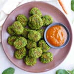 Homemade veggie tots on a plate with dipping sauce next to a carrot and spinach.