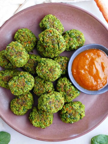 Homemade veggie tots on a plate with dipping sauce next to a carrot and spinach.