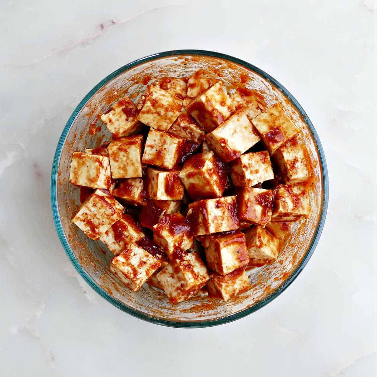 Marinated tofu in bbq sauce in a glass mixing bowl.
