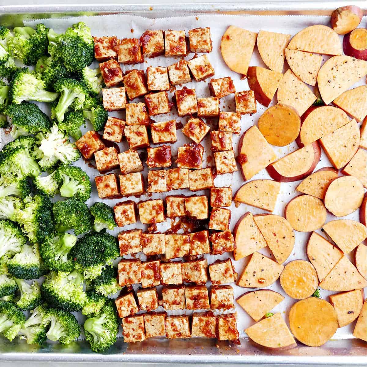 Broccoli, yams, and bbq marinated tofu on a baking sheet before cooking.