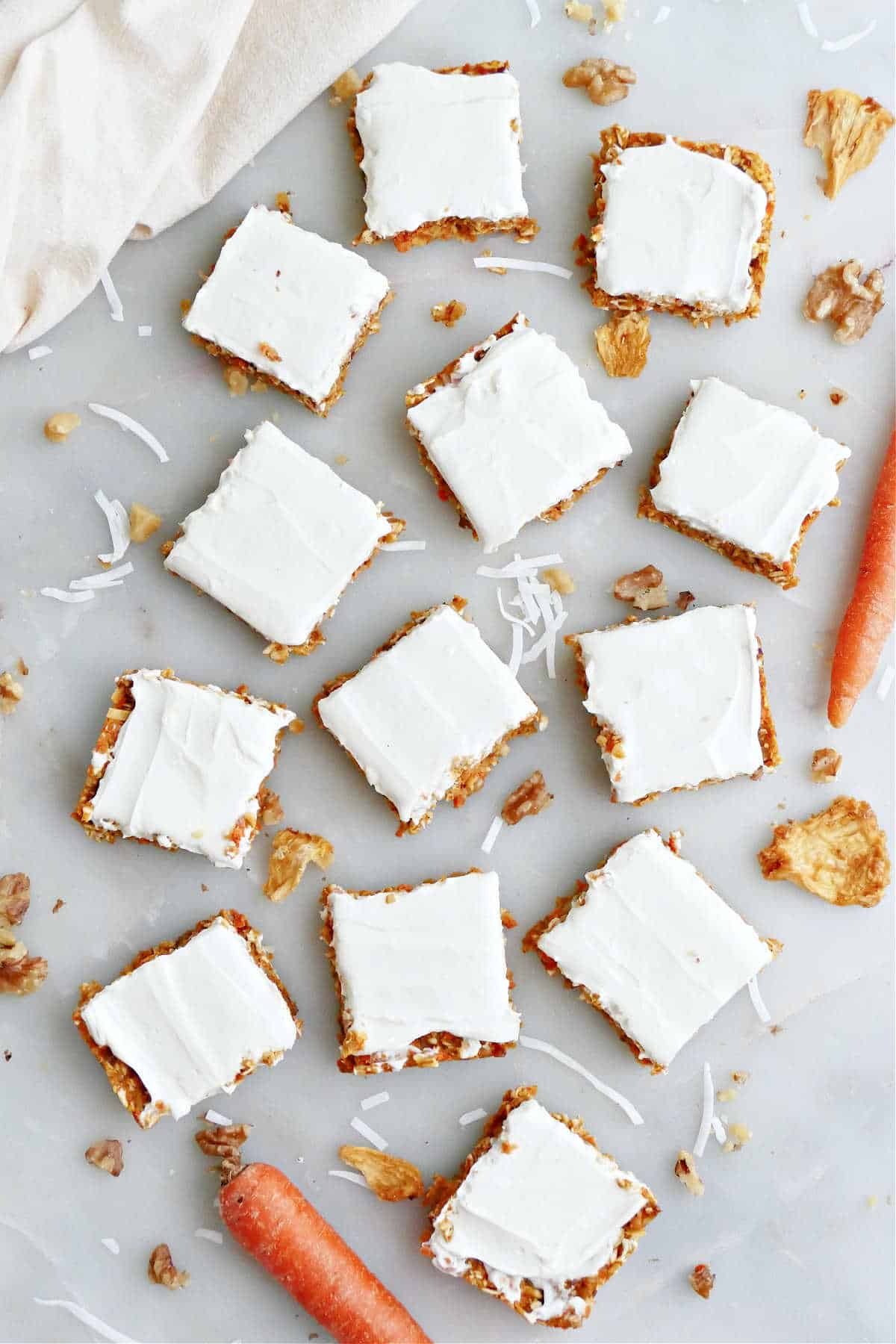 Several no bake carrot cake bars sliced into squares next to fresh whole carrots.