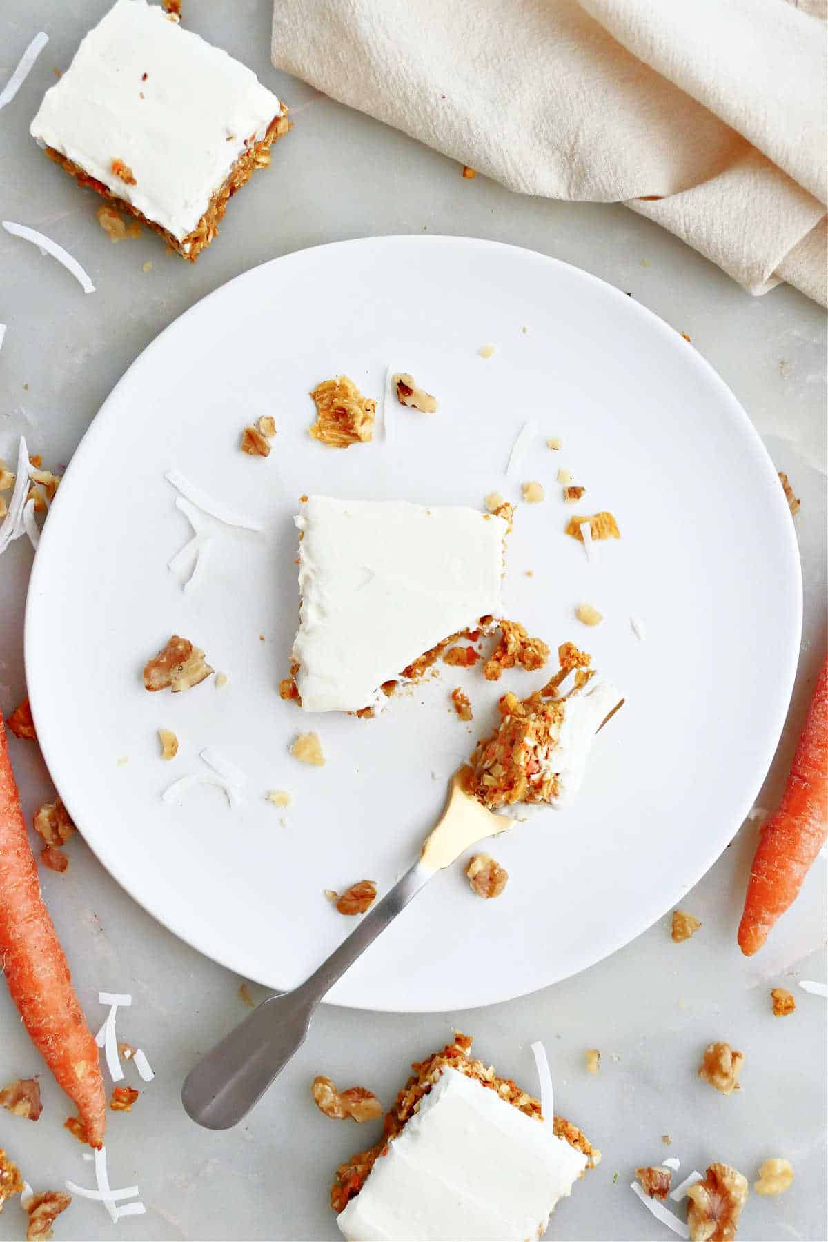 A frosted no bake carrot cake bar on white plate with a fork.