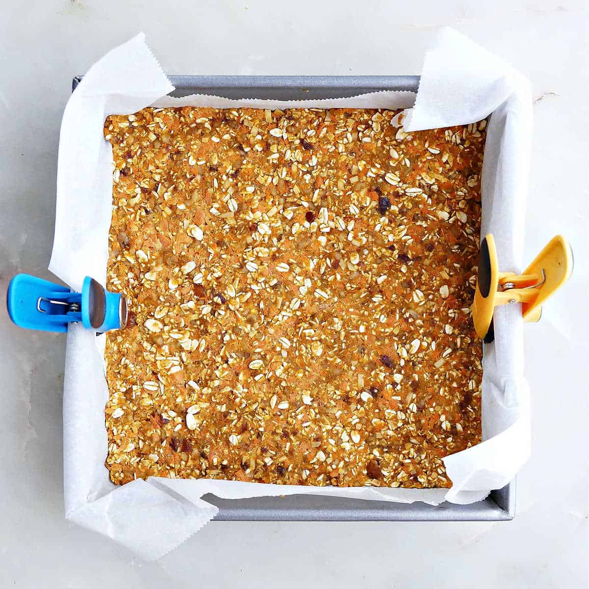 Healthy carrot cake bars in a square baking pan lined with parchment paper.